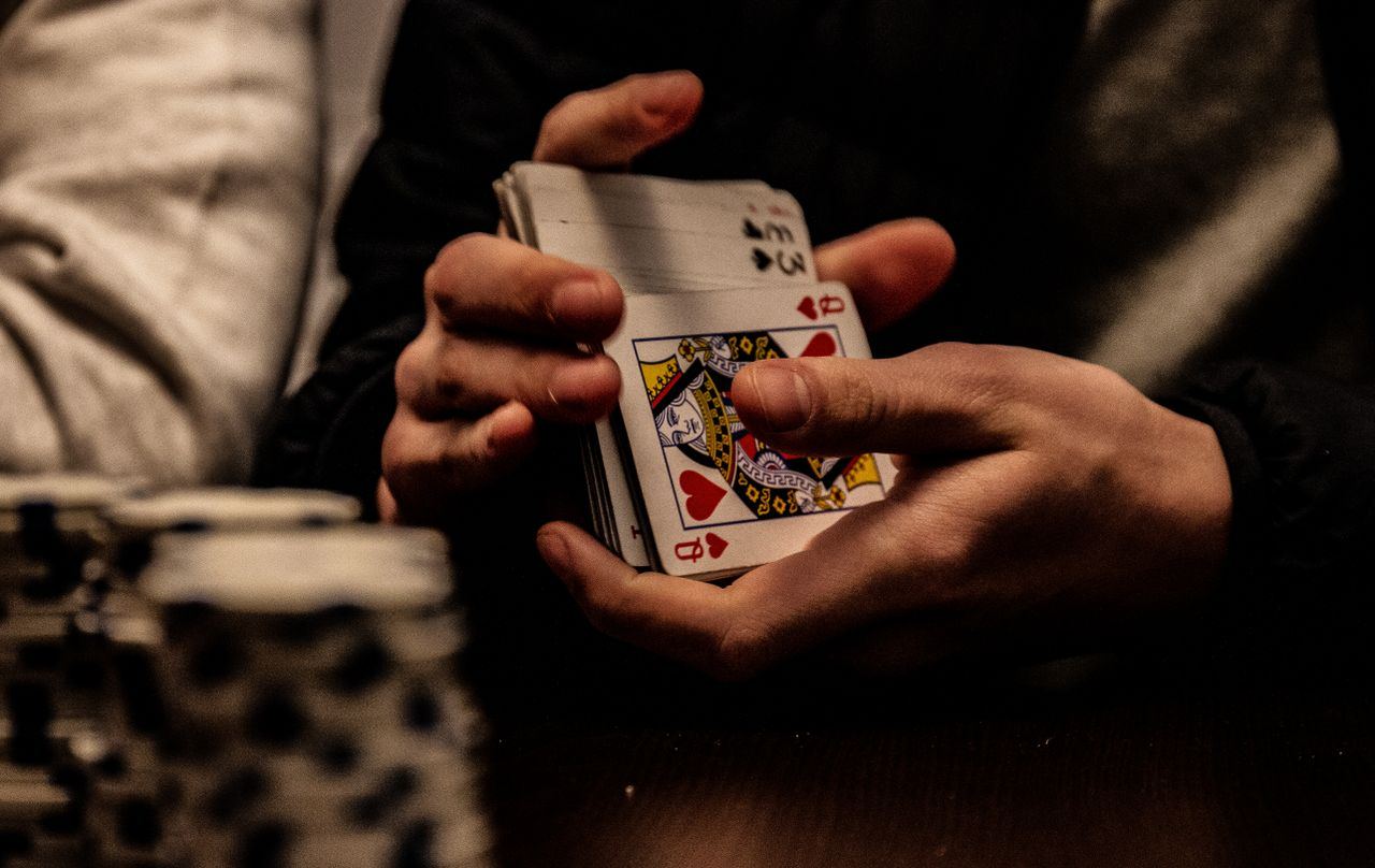 Tangan memegang tumpukan kartu dengan kartu As Hati di depan chip poker